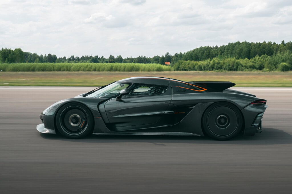 side shot of the Koenigsegg Jesko Absolut on a racetrack with clouds in sky and trees in background