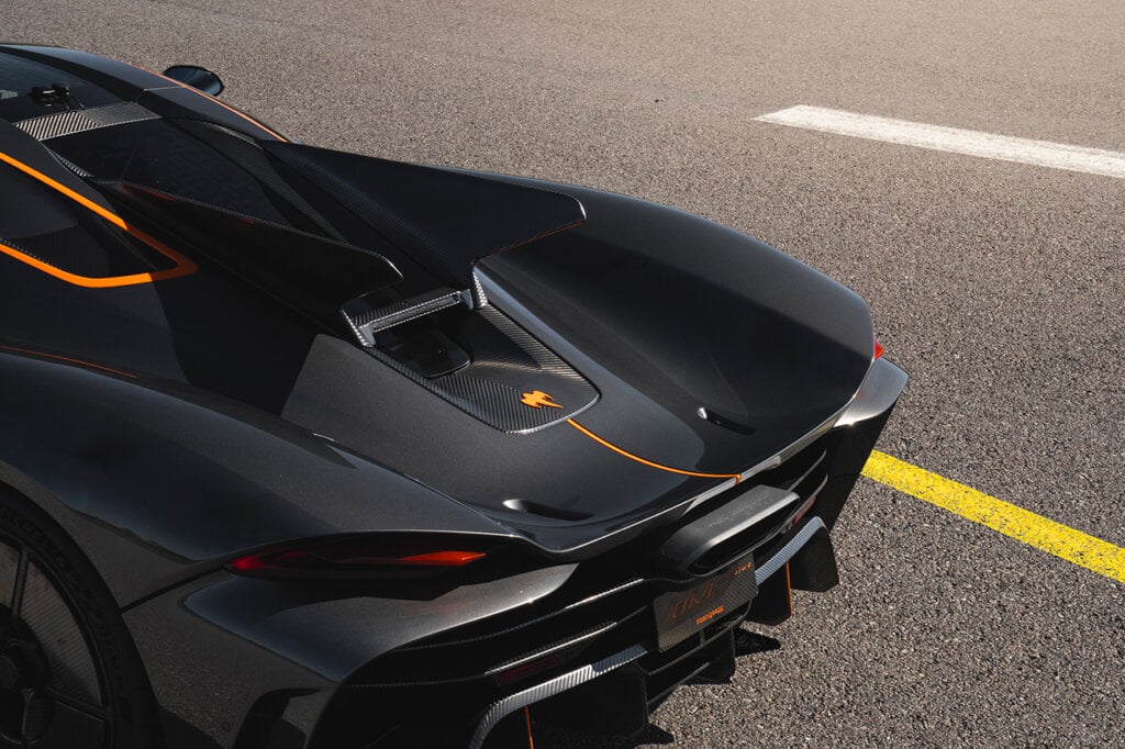 rear end of a black koenigsegg car with orange and carbon fiber accents
