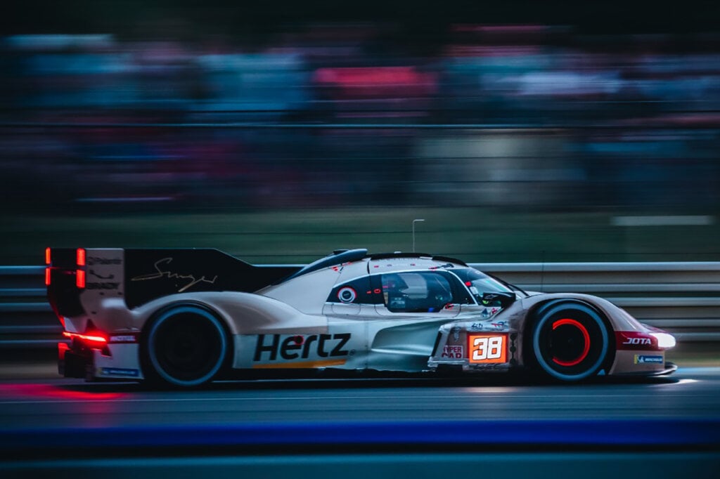 Modern Porsche Hertz hypercar with lights on during blue hour of 24hrs of Le Mans race.